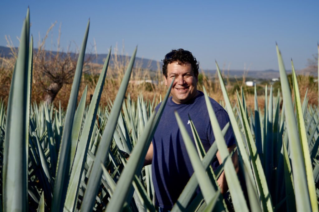 Chef Marcus 'Doc Agave' Guiliano standing in a field of Blue Weber Agave plants, verifying the raw material source for additive-free tequila